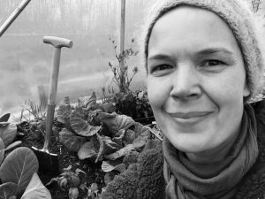 Svartvit bild av Sara i tunnelväxthuset. Bakom syns en liten spade och stora buckliga bladkål.
