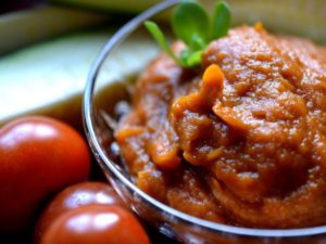 En skål med röd salsa står bredvid glansiga tomater inne i köket.