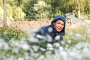 Sara sitter med luvtröja i en bädd av vite blommor och tittar upp kort.