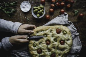 Focaccia, Två händer skär upp ett fantastiskt, platt bröd med tomater i.