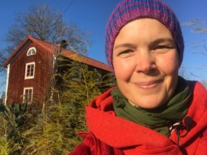 Sara i röd jacka och stickad mössa i rött och lila tittar glad in i kameran.
