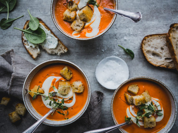 Flera tallrikar med rödorange tomapsoppa, smörgås och creme fraiche.