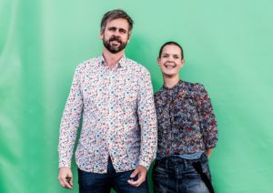 Sara och Johannes i blommiga kläder mot en turkos bakgrund.