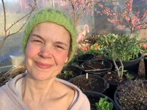 Sara i grön mössa med rosablommande fruktträd i bakgrunden.