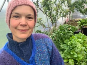 Sara i tre lager stickat njuter av ett grönt tunnelväxthus.