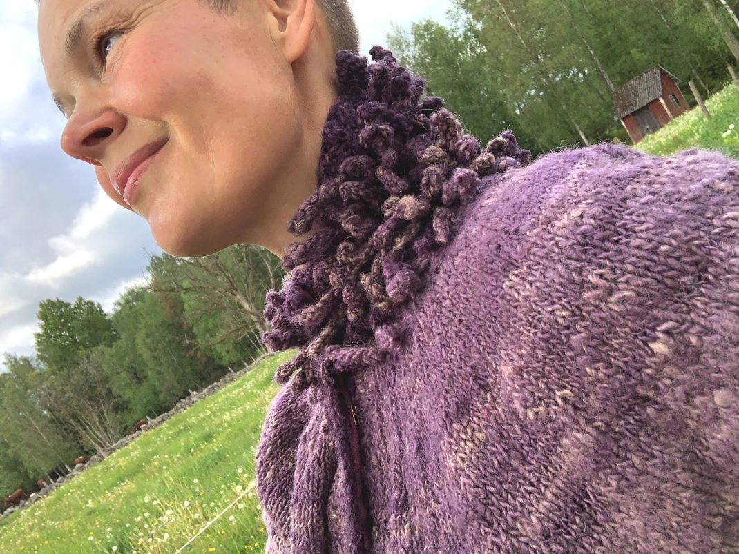 Sara står upp och tittar ut över kohagen och visar tröjans ok. My puff sleeve cardigan. 