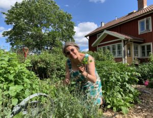 En kvinna i grön mönstrad klänning stor bredvid en bädd med kryddor