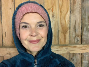 Sara i mössa och varm tröja i vedboden.