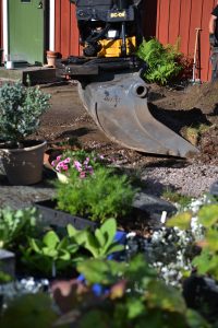 Närbild på en skopa som jobbar, med krukor med blommor i förgrunden.