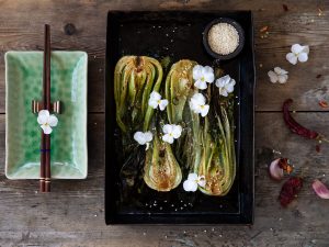 Ugnsrostad pak choi på en plåt med blommor och sesamfrön.
