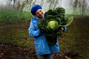 En tjej i blå jacka håller ett stort kålhuvud.